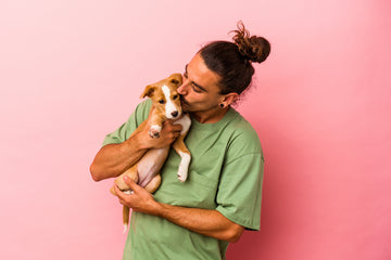 Young man with bun holding and kissing puppy 